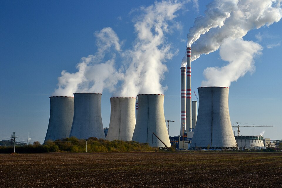 Coal power plant with massive cooling towers releasing thick white steam and black smoke from tall stacks
